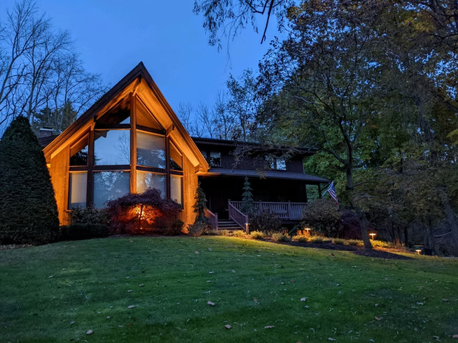 Beautifully lit A-frame home with warm landscape lighting at dusk in Pittsburgh