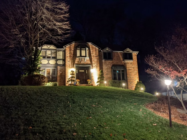 Tudor style brick home illuminated with professional outdoor lighting
